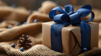 Elegant gift box wrapped in kraft paper with navy blue ribbon bow, pine cones and winter holiday decorations on rustic wooden background. For festive occasions.