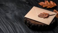 Kraft paper envelope with dried autumn oak leaf on rustic wooden slice against dark textured background, creating moody atmospheric composition.