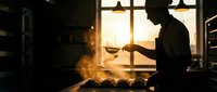 Silhouetted chef tossing food in a hot pan with dramatic flames and steam rising in a professional kitchen during golden hour lighting.