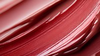 Smooth red lipstick or lip gloss texture with creamy swirled strokes creating elegant makeup cosmetic background for beauty and fashion applications.