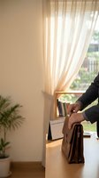 Professional businessman opening leather briefcase at home office desk near window with warm natural light and plants creating productive workspace atmosphere.
