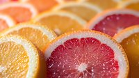 Fresh citrus slices arranged in rows showing vibrant cross sections of orange and pink grapefruit with juicy pulp and natural texture patterns.