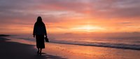 Woman in silhouette walking on beach at golden hour sunset, holding shoes, contemplative mood, travel and lifestyle concept for wellness and freedom themes.