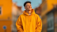 Happy young mixed-race man in bright orange hoodie laughing outdoors with warm sunset lighting and urban background for lifestyle marketing.
