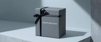 Elegant gray gift box with black ribbon and Happy Birthday inscription on minimalist light background, perfect for celebration concepts.