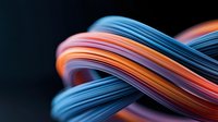 Vibrant twisted cables in blue, orange and pink colors intertwined against dark background create dynamic flowing curves and modern technological composition.