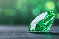 Sparkling emerald green gemstone on dark surface with soft bokeh background, showcasing luxury jewelry and precious stone brilliance in natural lighting.