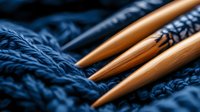 Wooden knitting needles on dark blue wool yarn texture with shallow depth of field. Close up macro shot showing crafting tools and textile details.