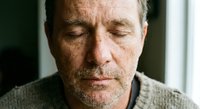 Mature Caucasian man with closed eyes in peaceful meditation or contemplation, showing serene facial expression and natural aging process indoors.