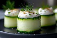 Fresh cucumber rolls filled with cream cheese, topped with herbs and spices on black plate. Elegant appetizer for catering and fine dining events.