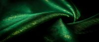 Luxurious emerald green silk fabric with golden shimmer creates elegant flowing waves and soft folds for premium textile and fashion design projects.