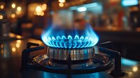 Blue gas flame burning on modern stove burner with blurred kitchen background and warm bokeh lights, demonstrating clean energy and cooking concept.