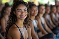Young mixed-race woman with curly hair smiling in fitness class with diverse group of people exercising together in bright gym studio for wellness.
