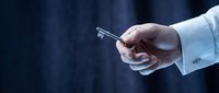 Businessman in light blue shirt holding silver key against dark blue background, symbolizing success, opportunity, and business solutions.