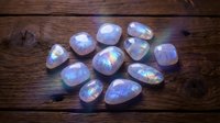Iridescent moonstone gemstones with rainbow flash arranged on rustic wooden surface for jewelry making and crystal healing practices.