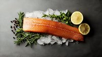 Raw salmon fillet on crushed ice with fresh rosemary sprigs, lemon slices and peppercorns against dark background, fresh seafood composition.
