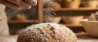 Hands dusting flour over fresh dough in a bakery kitchen, capturing the artisanal bread-making process with warm lighting and wooden surfaces.