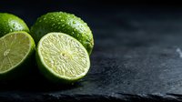 Fresh lime halves with water droplets on dark slate surface for culinary and beverage photography projects.