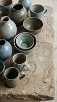 Handmade ceramic pottery collection with blue-green glazed bowls, mugs and vases arranged on rustic stone surface for artisan craft and home decor projects.