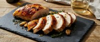 Sliced roasted duck breast with crispy skin served on slate plate with fresh rosemary and white wine for fine dining and culinary content.