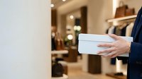 Male professional in dark business suit holding white envelope or document in hand, suitable for corporate communications, business correspondence, formal announcements.