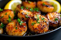 Pan seared sea scallops with caramelized crust garnished with fresh herbs and lemon slices served in cast iron skillet, close up view of gourmet seafood dish.