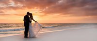 Romantic couple silhouette embracing on pristine beach during golden sunset with dramatic sky and gentle waves for wedding photography and love concepts.