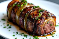 Juicy pork tenderloin sliced and garnished with fresh herbs, glazed with honey-soy sauce, served on white plate. Gourmet meat dish with caramelized onions.