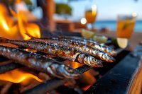 Grilled fish cooking over open flames on barbecue grill with drinks in background for outdoor dining and summer cooking experiences.
