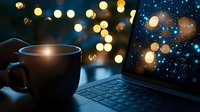 Steaming coffee cup next to laptop keyboard at night, with glowing bokeh lights and raindrops on window creating magical atmosphere for remote work or studying.