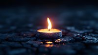 Glowing tea light candle burning in darkness on textured stone surface creates atmospheric mood with warm flame reflection and bokeh effect.