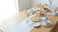 Elegant dining table setting with white porcelain dishes, wooden plates, and fresh flower arrangements in glass vases for home entertaining and hospitality.