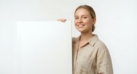 Young professional Caucasian woman in beige shirt smiling while holding blank white board for presentations, marketing campaigns and business announcements.