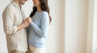 Young couple embracing intimately in bright modern home interior, man in beige shirt woman in blue sweater, romantic relationship lifestyle moment.