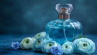 Elegant glass perfume bottle with blue fragrance surrounded by white ranunculus and delicate blue flowers on dark background, luxury beauty concept.