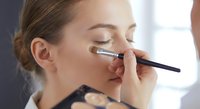 Young Caucasian woman getting professional makeup application with brush on face in beauty salon for cosmetic treatment and skincare routine.