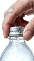 Close-up of hand opening water bottle cap with condensation droplets on glass, isolated on white background for beverage, hydration and refreshment concepts.