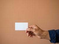 Caucasian male hand holding blank white business card against neutral beige background for branding, marketing, and corporate identity design projects.