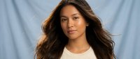 Young Asian woman with long flowing brown hair wearing white top against light blue fabric background for fashion and beauty concepts.