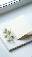Blank greeting card with white petite flowers and green stems on textured paper, positioned near window light for stationery, invitations, and correspondence design projects.