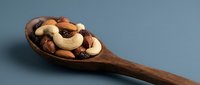 Mixed nuts and dried fruits in wooden spoon on neutral background for healthy snacking and cooking ingredients display.