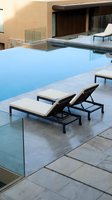 Modern luxury pool area with infinity edge, glass railings, contemporary lounge chairs on stone deck at upscale resort or residential property during golden hour.
