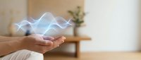Hands cupped holding glowing blue energy waves in modern living room interior. Digital technology concept for healing, meditation, and spiritual wellness.