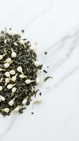Loose leaf green tea blend with jasmine flowers and dried botanicals scattered on white marble surface for beverage and wellness design projects.