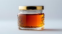 Glass jar with golden lid containing amber liquid, featuring diamond pattern texture, illuminated against light background. Suitable for honey, syrup or preserves packaging.