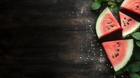 Fresh juicy watermelon slices with green leaves and salt scattered on dark rustic wooden background with copy space for summer menu design.