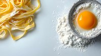 Fresh raw egg yolk in flour and uncooked pasta noodles on light background, culinary composition for homemade Italian cuisine preparation.