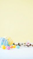 Colorful Easter eggs and jelly beans scattered on white surface with pastel yellow background for spring holiday celebration and festive decoration projects.