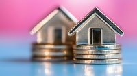 Miniature wooden houses sitting on stacks of coins against pink background representing real estate investment, mortgage, property market concept.