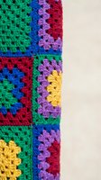 Colorful crochet granny squares in vibrant rainbow colors showing detailed handmade textile craftsmanship for creative projects and home decor applications.